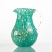 Spotted glass pitcher, marine green with red, yellow, white speckles, rounded bulbous shape, curved handle, glossy reflective surface.