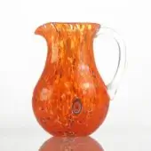 Hand-blown glass pitcher, orange with mottled speckles, rounded bulbous shape with flared spout and clear curved handle.