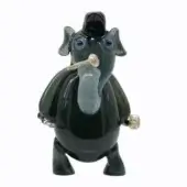 Glass dog sculpture, dark grey-green translucent glass, rounded form with blue eyes, black hat, holding clear glass pipe, glossy finish.