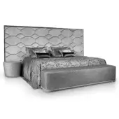 King bed with light gray velvet hexagonal headboard, silver duvet, textured bench, and round side table in studio setting.