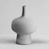 Ceramic vase, matte gray, organic bulbous shape with slender neck on cylindrical pedestal, displayed against white wall.