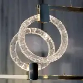 Chandelier, transparent methacrylate, interlocking cracked rings with black and gold metal accents, warm diffused light, blurred gray background.