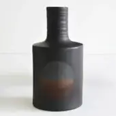 Ceramic vase, dark gray, cylindrical with flared rim; recessed circular area displays reddish-brown to orange gradient, matte finish with vertical striations.