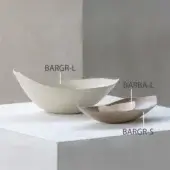 Beige and gold nesting bowls, matte ceramic, asymmetrical shape, arranged on light gray cube surface against gray wall backdrop.