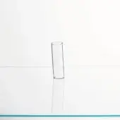 Glass cylinder on white surface, elongated shadow, transparent material, minimalist composition, turquoise line accent, studio lighting.