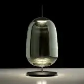 Emerald green glass table lamp, ridged oval shade, polished metal stem, black base, warm diffused light, gray surface reflection.