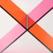 Geometric glass panels in pink and orange create an abstract cross shape against white, with dark gray metal framing and diffused lighting.