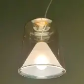 Pendant lamp, amber glass, cylindrical shade with frosted white inner cone, suspended from white cord against olive green wall.