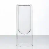 Transparent double-walled glass vessel, cylindrical shape, rounded base, minimalist design, clear glass, reflective gray surface, white background.