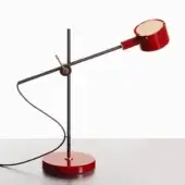 Scarlet red desk lamp with matte black support, circular base, and brass accents; adjustable arm with cylindrical glossy head on red surface.