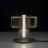 Rapanui table, gold finish, cylindrical base with translucent smoky grey glass tabletop and vertical accent rod.