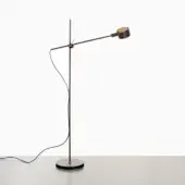 Black floor lamp with cylindrical shade, matte metal stem, and brass joint on gray surface against white backdrop.