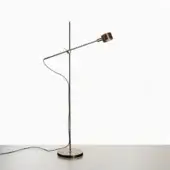 Floor lamp, anodic bronze, with slender cylindrical stem and curved articulated arm, on dark gray surface against white backdrop.