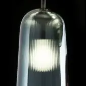 Pendant light, green glass, cylindrical shade with vertical ribbing and inner diffuser, chrome mounting fixture, studio shot.