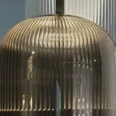 Metallized pendant lamp with ribbed, spherical shape and polished golden finish reflecting architectural details against a gray backdrop.