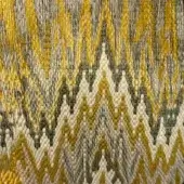 Geometric textile with zigzag pattern in olive green, creamy white, and mustard yellow; dense weave with visible, textured threads.