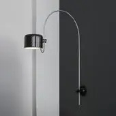 Arc lamp, black metal, with perforated shade and chrome arm, mounted on light and dark gray walls in studio setting.