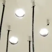 Recessed ceiling lights with metallic rings, pale beige surface, black woven conduit, bright white illumination, modern architectural detail.