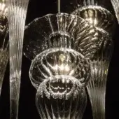 Glass chandelier with clear, rippled glass bulbs and slender rods, featuring warm internal lighting and etched “opera turandot clear” text.