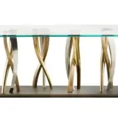 Clear glass table with sculptural base featuring intersecting brushed silver and polished brass metal legs, studio shot.