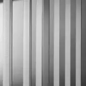 Metal slat screen with vertical grain, grayscale tones, and rhythmic light-shadow pattern; decorative architectural element.