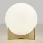 Table lamp, satin brass, arched base supports a white opaque sphere; Terzani Oscar model on reflective surface, studio lighting.