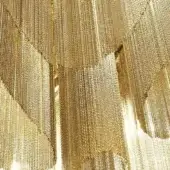 Gold-plated chain curtain with layered strands, creating a dense, textured composition of reflective metallic tiers and overlapping sections.