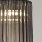 Glass pendant light, smoky gray, cylindrical with fluted rods and warm white illumination, metallic band detail, studio setting.