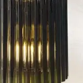 Glass pendant light, smoky gray-green, with vertical rods and exposed Edison bulbs emitting a warm amber glow in a dense columnar form.