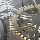Gear mechanism with gold and chrome finishes, clear glass top, and mesh base, displaying intricate layered construction and metallic reflections.
