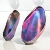 Abstract glass sculptures, pink, purple, and blue marbled glass, elongated organic forms displayed on a white surface.