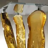 Abstract amber sculptures, translucent resin or glass, vertical striations on a clear glass shelf with silver metal frame.