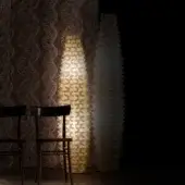 Gold floor lamp with geometric panels and textured light projection, black chairs, dark brown woven wall, black wall.