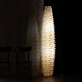 Floor lamp, off-white metal, geometric cactus shade casts patterned shadows on beige textured wallpaper, with minimalist chairs visible.