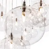 Glass sphere chandelier with Edison bulbs, brushed silver rods, and tiered arrangement, emitting warm light against a neutral backdrop.