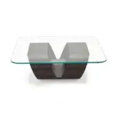 Coffee table, clear glass top, dark gray metal base with angular forms and central V-shaped cutout, beveled edges, matte finish.