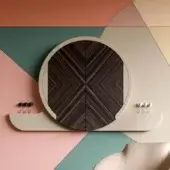 Vismara dart board cabinet, cream and dark wood, circular shape with radiating diamond veneer pattern and brass knobs, against geometric wall.