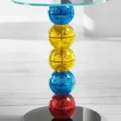 Glass table with stacked, spherical orbs in blue, yellow, and red, featuring a clear glass circular tabletop and dark metal plate.