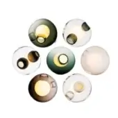 Spherical wall lights in clear, brown, green & white glass display circular openings & embedded inclusions against a white backdrop.