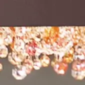 Chandelier with faceted glass spheres in amber, orange, and clear tones suspended from a dark metal horizontal frame, creating layered illumination.