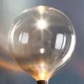 Sofi amber light bulb, clear glass with amber tint, spherical shape displaying warm orange filament glow against blurred dark blue-grey.