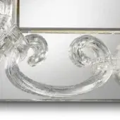 Glass sculpture within a silvered, multi-panel mirrored frame; baroque swirls create a transparent, reflective decorative element.