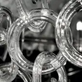 Transparent glass sculpture with looping circular forms, reflective surface, and internal bubbles, displayed against a dark background.