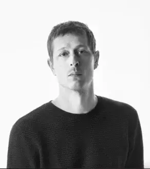 Grayscale portrait of a young man with short dark hair wearing a dark knit sweater against a light gray background
