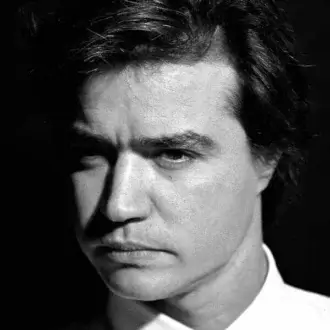 Close-up black and white portrait of a man with dark hair and intense gaze against a dark background