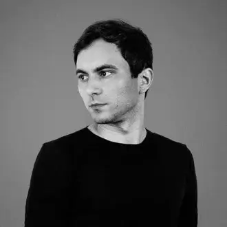 Grayscale portrait of a person with short dark hair looking to the side wearing a dark long-sleeved shirt against a gray background