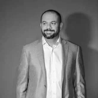Portrait of Filippo Mambretti, a man in a light shirt and gray tweed blazer, against a dark gray backdrop with soft, even lighting.