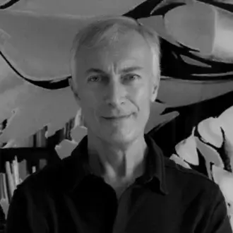 Marco Lucchi portrait with abstract black and white artwork backdrop, stacked papers, soft studio lighting, gray hair, button-down shirt.