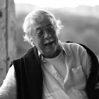 Black and white portrait of Ben Swildens, elderly man with white hair, glasses, and shawl, soft focus outdoor background.
