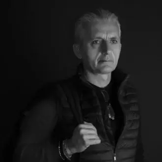 Black and white portrait of Michele Losito wearing a black crewneck shirt and quilted puffer vest with silver bracelets.